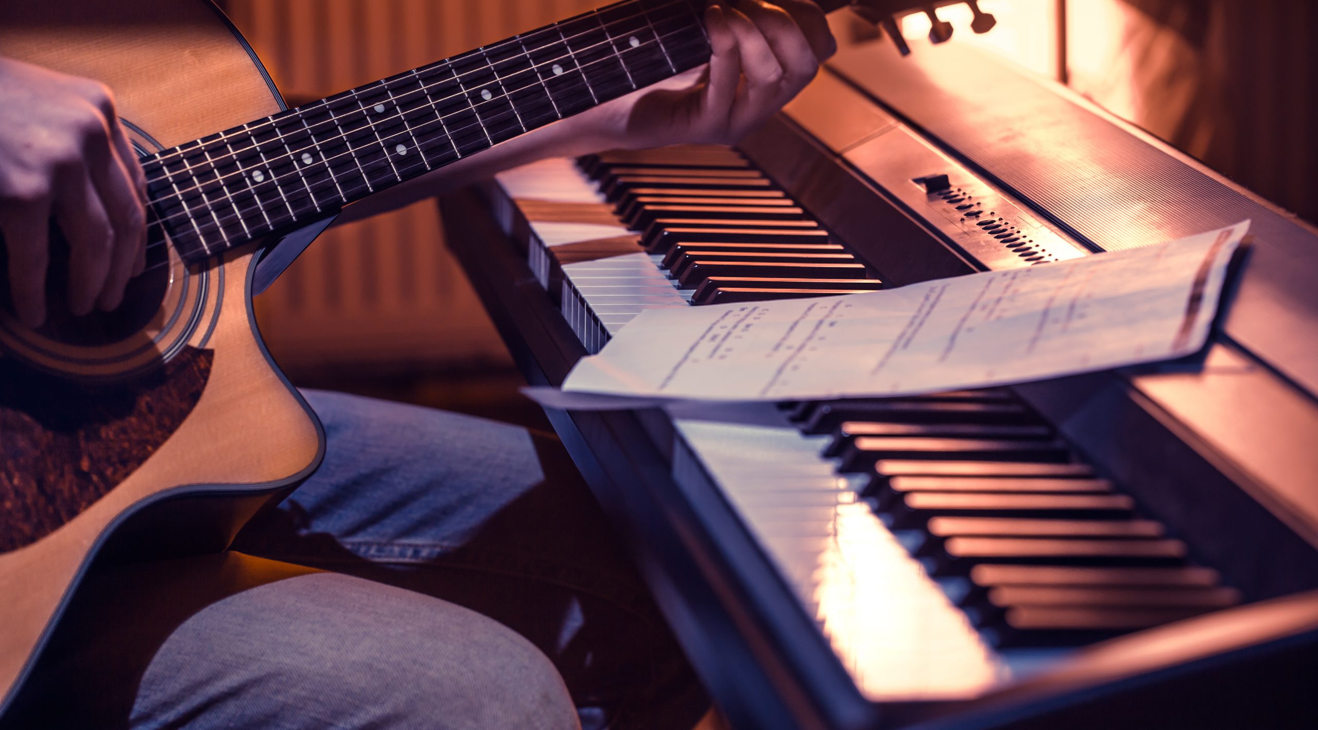 man playing acoustic guitar and piano close-up, recording notes